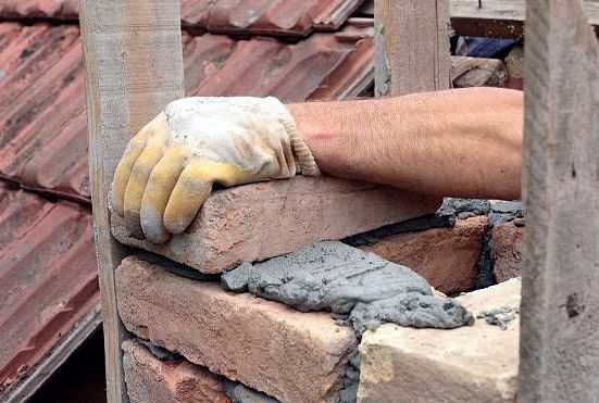 Gloved mason bedding a brick course on fresh mortar